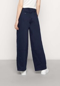 Marinblå vida byxor i mjukt tyg med en slät yta, som har bakfickor och hög midja.