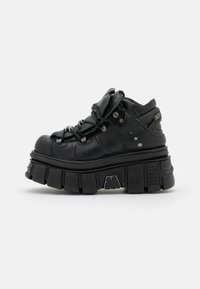 Black chunky platform sneakers with rounded toe, textured leather upper, padded tongue, and metallic accents; thick ridged sole design.