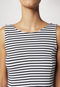 Czarno-biała, paskowana bluzka bez rękawów z okrągłym dekoltem, wykonana z teksturowanej tkaniny i dopasowanego kroju, podkreślająca pionowe zaszewki.