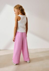 Hvid tanktop parret med pink og hvid ternede wide-leg bukser. Stoffet virker tekstureret, med en afslappet pasform og enkle sko.