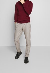 Burgunderfarbener Rollkragenpullover kombiniert mit hellgrauen strukturierten Hosen und schwarzen Schnürschuhen, die ein entspanntes, lässiges Outfit präsentieren.