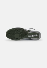 Grå och grön sneakersula med ett texturerat mönster. "Reebok"-logotyp i vitt på hälen, som framhäver mönstret för grepp.