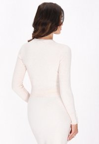 Helles beige Langarmshirt mit geripptem Textur, tailliertem Design und gewellten Bündchen. Weicher Stoff mit einem dezent gemusterten Effekt für zusätzliche Details.