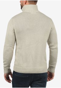 Licht beige gebreide trui met een hoge kraag. Ribgebreide manchetten en zoom. Gelaagde stof, aansluitend ontwerp en naadloze schouderconstructie.