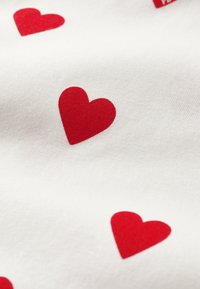 Tessuto di cotone con uno sfondo bianco e cuori rossi sparsi. I cuori sono lisci e piatti contro la superficie tessurizzata.