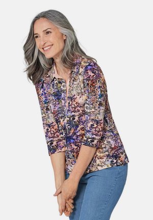Bunt gemusterte Bluse mit Dreiviertelärmeln, die ein lebhaftes Blumen- und abstraktes Muster in Pink-, Lila- und Blautönen zeigt.