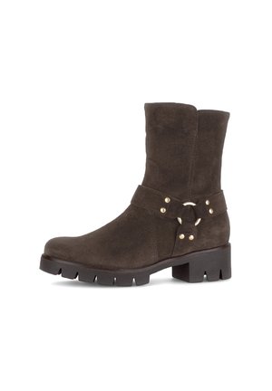 Bottine en suède marron foncé avec une semelle épaisse, une sangle avec un anneau en métal et des accents en or. Texture lisse et design de hauteur intermédiaire.