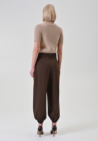 Top in maglia a costine beige con maniche corte, abbinato a pantaloni a vita alta marroni con righe sottili, polsini elasticizzati e tacchi neri lucidi.