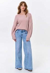 Helles rosa, geripptes Sweatshirt mit lockeren Ärmeln, kombiniert mit hoch taillierten, weit geschnittenen hellblauen Jeans, die dezente Nähte und große Säume aufweisen.