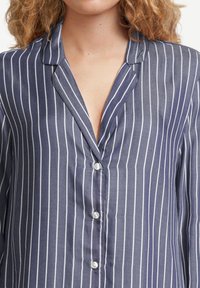 Camicia a righe navy con righe verticali bianche, dotata di colletto, texture morbida e bottoni simili a perle.