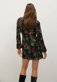 Kurzes Blumenkleid mit langen Ärmeln und dunklem Hintergrund, versehen mit lebhaften roten und grünen Mustern. Hergestellt aus glattem, leichtem Stoff.