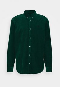 Zielona koszula sztruksowa na guziki z długimi rękawami, spiczastym kołnierzykiem i białymi guzikami. Na lewej piersi subtelne logo.