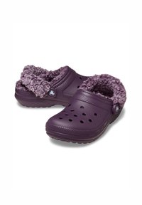 Lila Clogs mit einem weichen, flauschigen Innenfutter, ausgestattet mit Belüftungsöffnungen im Obermaterial und einer strukturierten Sohle für optimalen Grip. Verstellbarer Seitenknopf.