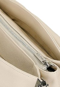 Beige leren handtas interieur met een gestructureerde afwerking, voorzien van een zilveren rits en een gelabelde zilveren tag. Twee zichtbare compartimenten.