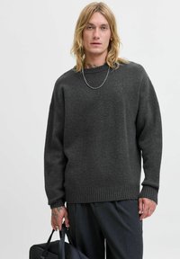 Mørkegrå strikket trøje med rund hals, ribbede manchetter og kant, parret med mørke bukser og en sort taske. Glat tekstur, afslappet pasform.