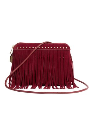 Červená semišová crossbody taška s dlhými strapcami a zlatými cvokmi pozdĺž hornej hrany, s tenkým ramenným popruhom a zipsovým zatváraním.