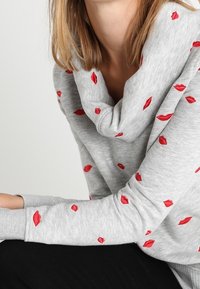 Grauer Pullover mit Schalkragen, versehen mit verstreuten roten Lippenabdrücken. Weicher Stoff und lockere Passform, mit langen Ärmeln und gerippten Bündchen.