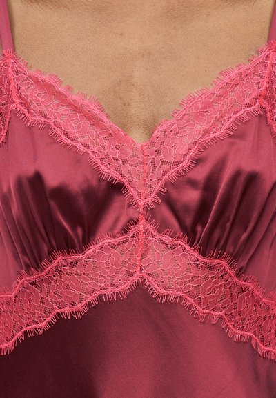 Κοντινό πλάνο ενός ενδύματος από βελούδινο σατέν μπορντό με ροζ δαντέλα με λουλούδια γύρω από το V-λευκό ντεκολτέ και την περιοχή του στήθους.