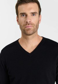 Zwarte V-hals trui met geribbelde details op de schouders, gebreide textuur en een aansluitend silhouet. Eenvoudig, klassiek ontwerp geschikt voor casual dragen.