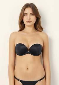 Zwarte strapless beha van gladde stof, met een uitgesneden ontwerp in het midden en contrasterende hardware accenten. Getextureerde bikini broek met verstelbare banden.