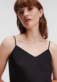 Top satin negru fără mâneci, cu un decolteu în V, bretele subțiri și o textură netedă, evidențiind un stil elegant și minimalist.