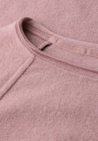 Un tissu de sweatshirt rose clair avec une surface texturée, présentant un col arrondi et un col côtelé. Détails de couture visibles.