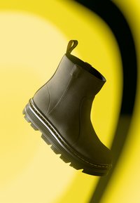 Bottine en cuir grise avec finition texturée, bout arrondi et semelle en caoutchouc noir robuste dotée d'un profil en zigzag et de surpiqûres jaunes.