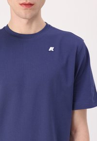 Navy blue cotton t-shirt with a round neck, short sleeves, and a small white logo embroidered near the left shoulder. Smooth texture.