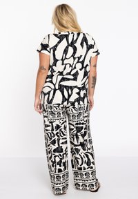 Haut noir et blanc à motifs, ample, à manches courtes, associé à un pantalon large avec un imprimé complexe et des motifs contrastés.