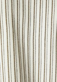 Vävt tyg med vertikala ränder i off-white och metallisk guld. Texturen är lätt upphöjd och skapar ett mönstrat utseende.