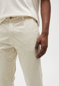 Pantaloni beige in cotone con una vestibilità rilassata, dotati di tasche laterali, una superficie liscia e chiusura con bottone in vita.