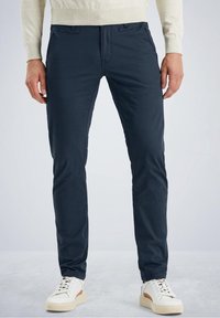 Chino in cotone blu navy con vestibilità slim, dotati di tasche frontali, passanti per cintura e una texture liscia, abbinati a sneakers bianche.