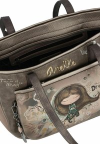 Helle braune Handtasche mit strukturiertem Finish, ausgestattet mit einer Fronttasche, die eine Illustration und den Text "Du bist aus Magie gemacht" zeigt. Goldene Hardware-Akzente.
