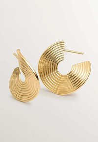 Pendientes en tono dorado con un diseño curvado y estrías concéntricas. Un pendiente es más grande que el otro, y ambos tienen un acabado metálico suave.