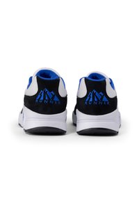 Zapatillas deportivas en blanco y negro con acentos en azul, que cuentan con una parte superior de ante y malla, un collar acolchado y un logotipo prominente en el talón.