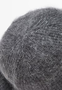 Berretto lavorato a maglia grigio realizzato in materiale morbido e peloso. Presenta un motivo testurizzato con una forma rotonda e leggere variazioni di colore.