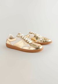 Gold metallic leather sneakers with white accents, flat laces, rubber sole, and a textured finish on the upper part.