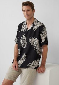 Korte mouwen zwarte shirt met wit palmenbladpatroon; lichtgewicht stof; knoopsluiting aan de voorkant; gecombineerd met beige shorts.