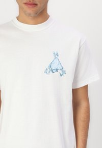 Balta medvilninė marškinėliai su šviesiai mėlyna grafika, vaizduojančia kalną, aplink kurį yra blokinio stiliaus raidės "H", "U" ir "F". Trumpi rankovės.