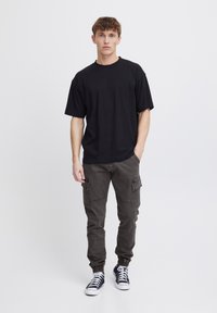 Black short-sleeve t-shirt paired with dark gray cargo pants featuring side pockets and elastic cuffs, complemented by black and white sneakers.