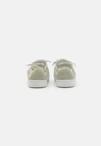 Grønne lerretssneakers med hvite gummisåler, rund form, elastiske lisser og myk tekstur. Har et lite baklogo-accent.