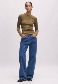 Olijfgroene geribbelde lange mouwen top gecombineerd met wijde blauwe jeans. De outfit heeft een aansluitende silhouette en een soepele textuur. Zwarte schoenen maken de look af.