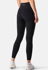 Leggings de sport noirs avec une taille haute, dotés d'une texture lisse, d'un design ajusté et d'un branding minimal à l'arrière.