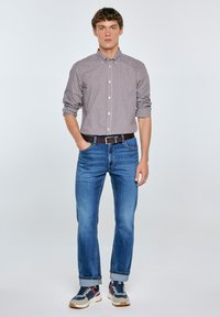Camisa de cuadros de botones en rojo y blanco; jeans rectos azules; cinturón marrón; zapatillas deportivas con acentos en azul, rojo y blanco; puños remangados.