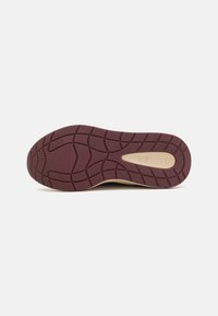 Semelle de chaussure en caoutchouc bordeaux avec motifs antidérapants texturés et un accent beige affichant le nom de la marque "Guess".