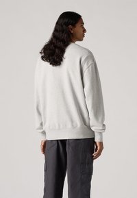 Felpa leggera grigia a girocollo con polsini e orlo a costine, caratterizzata da un tessuto texturizzato. Indossata con pantaloni cargo scuri.
