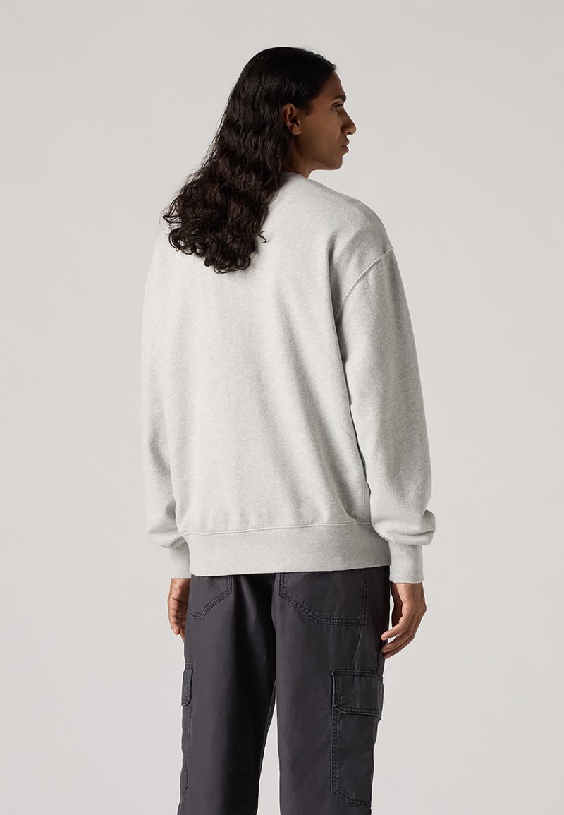 Felpa leggera grigia a girocollo con polsini e orlo a costine, caratterizzata da un tessuto texturizzato. Indossata con pantaloni cargo scuri.