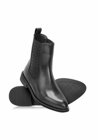 Czarne skórzane botki Chelsea z teksturowanymi elastycznymi panelami po bokach i żłobioną gumową podeszwą, wyeksponowane na białym tle.