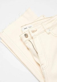 Jeans beige chiaro con leggero sfilacciamento all'orlo, dotati di cerniera frontale, bottone metallico e dettagli di cucitura minimalista.