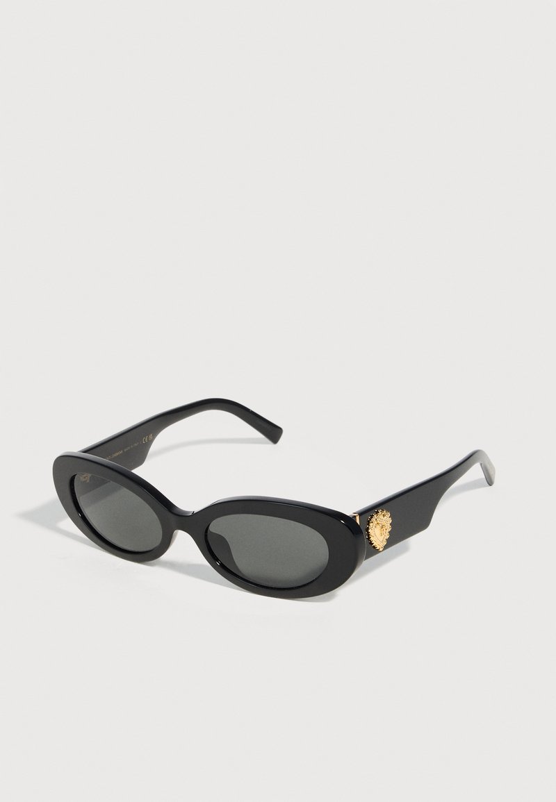 Μαύρα οβάλ γυαλιά ηλίου με σκουρόχρωμους φακούς και χρυσό έμβλημα λιονταριού στον βραχίονα, εμφανίζονται σε λευκό φόντο.
